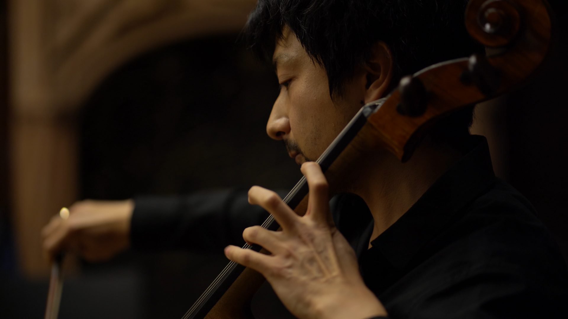 Cellist spielt konzentriert mit Bogen in dunkler Umgebung.