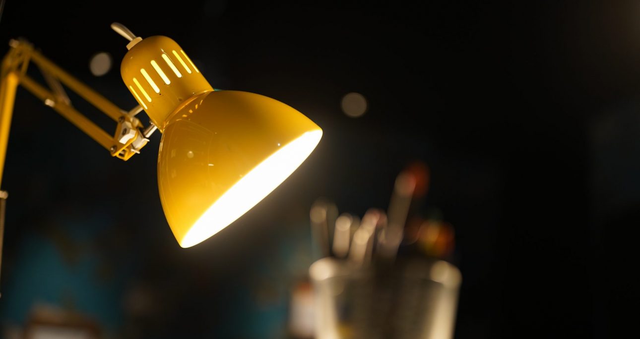 Gelbe Lampe leuchtet auf unscharfe Schreibutensilien im Hintergrund.