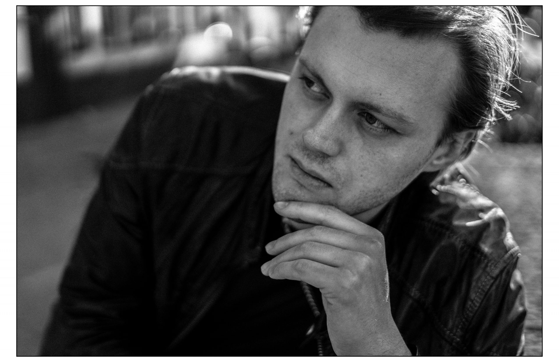 Mann in Lederjacke, nachdenklich zur Seite blickend, Schwarz-Weiß-Bild mit unscharfem Hintergrund.