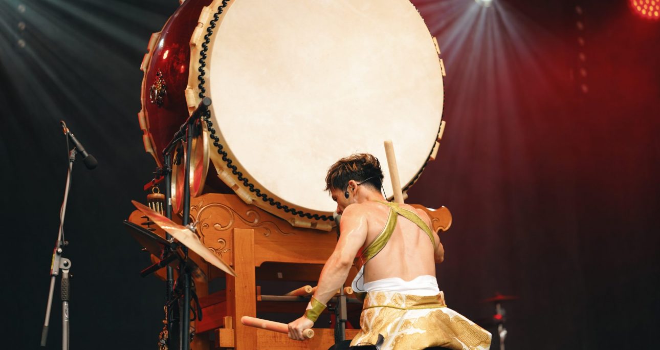 Musiker spielt auf großer traditioneller Trommel auf der Bühne im Scheinwerferlicht.