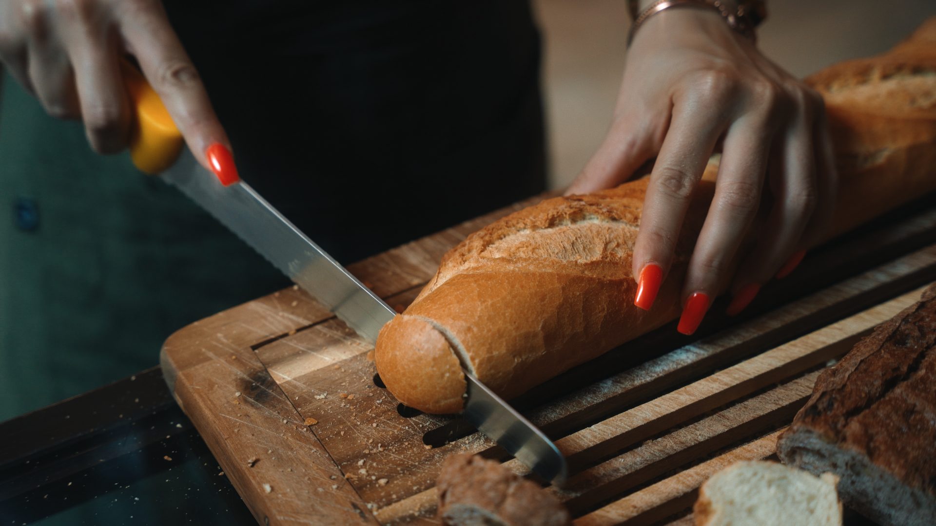 Person schneidet Baguette auf Holzbrett mit Brotmesser.